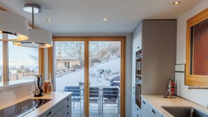 Una cocina moderna con un ventanal grande, una puerta corrediza de vidrio que da a un área exterior nevada y un horno empotrado.
