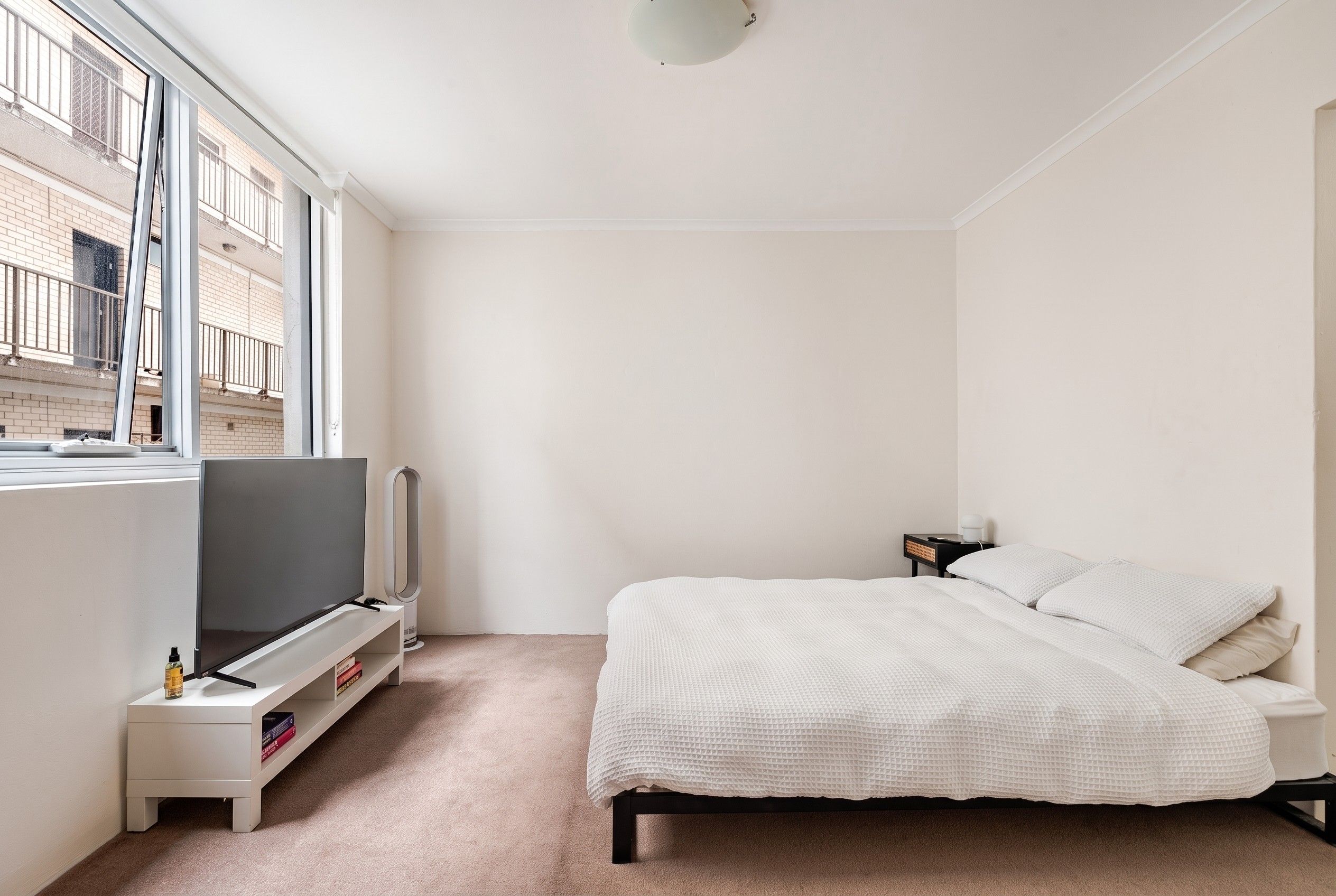 A minimalist bedroom with a bed, TV, and a small bedside table.