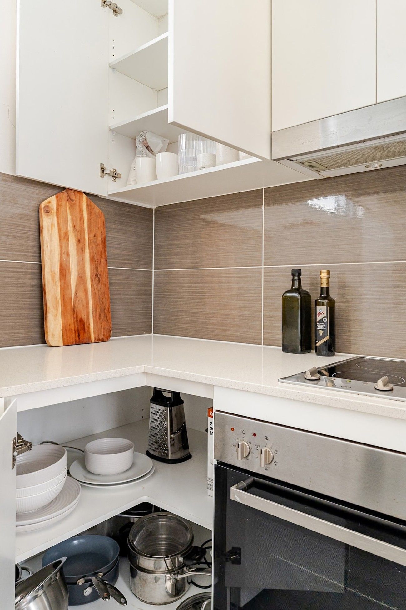A modern kitchen with white cabinetry, a wooden cutting board, two bottles of olive oil, and a built-in oven.