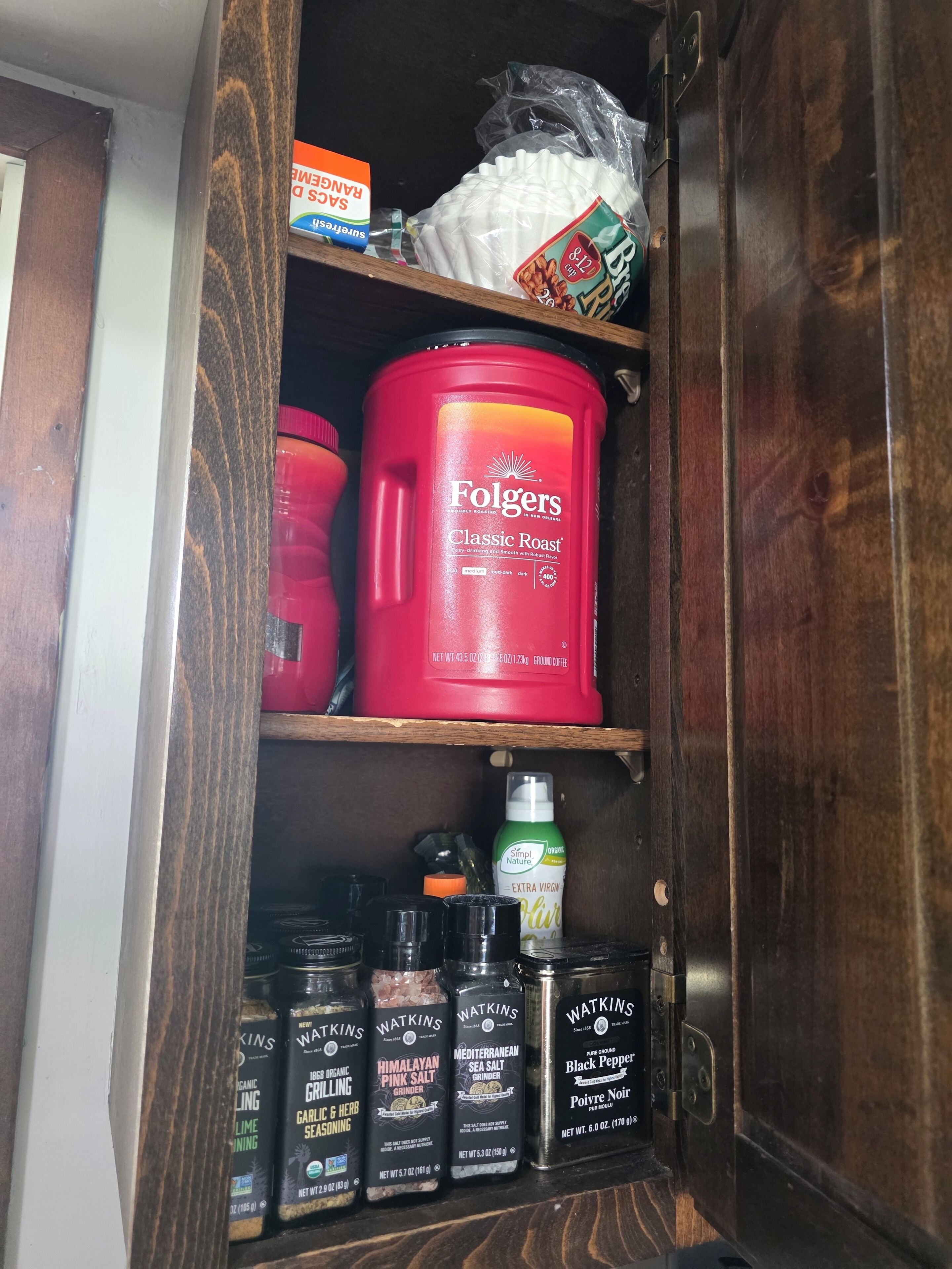 A kitchen cabinet with various food items including a red Folgers coffee canister, a bag of white sugar, and several spice containers.