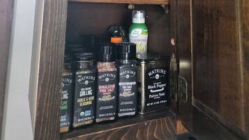 A kitchen cabinet with various food items including a red Folgers coffee canister, a bag of white sugar, and several spice containers.