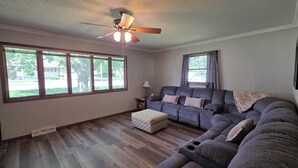 A living room with a sectional sofa, a ceiling fan, and large windows.