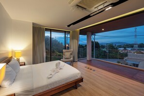A modern hotel room with a large bed, a view of the cityscape, and a balcony with a chair. - Tranquil 3-Storey Villa with Private Pool (Koh Samui)