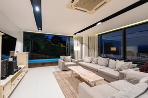 A modern living room with a large window, a flat-screen TV, a sofa set, and a coffee table. - Tranquil 3-Storey Villa with Private Pool (Koh Samui)