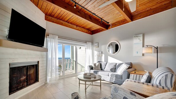 Una sala de estar moderna con chimenea, un televisor de pantalla plana montado en la pared, un conjunto de sofás, una mesa de centro y un ventanal con vistas al exterior.