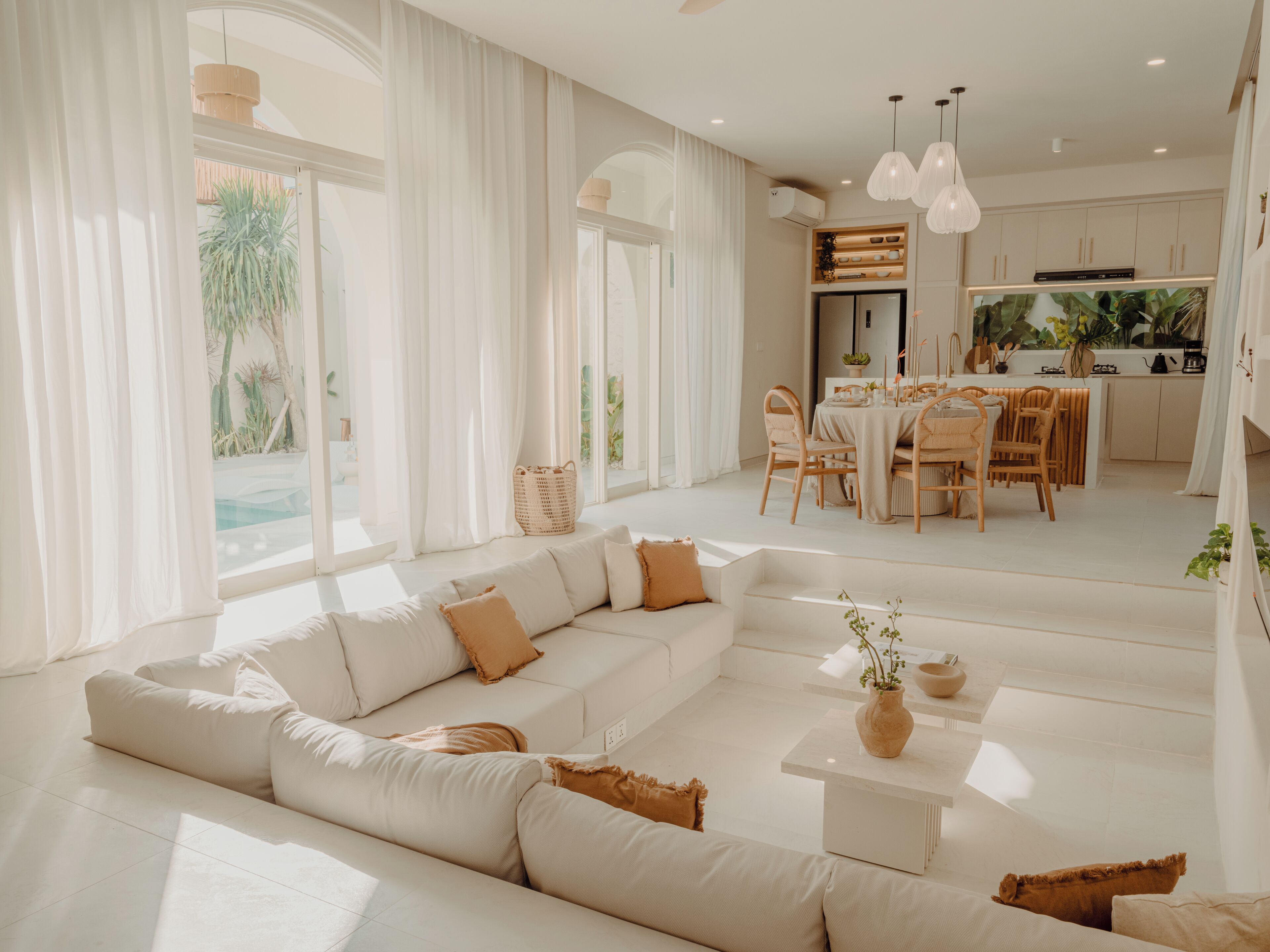 A modern living room with a large sectional sofa, a dining area, and a kitchen with pendant lighting.