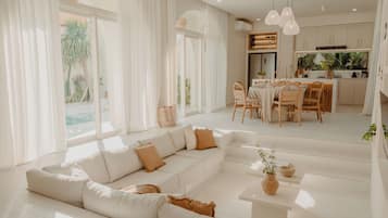 A modern living room with a large sectional sofa, a dining area, and a kitchen with pendant lighting.