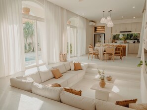 Un salon moderne doté d’un grand canapé d’angle, d’un coin repas et d’une cuisine avec des luminaires suspendus.