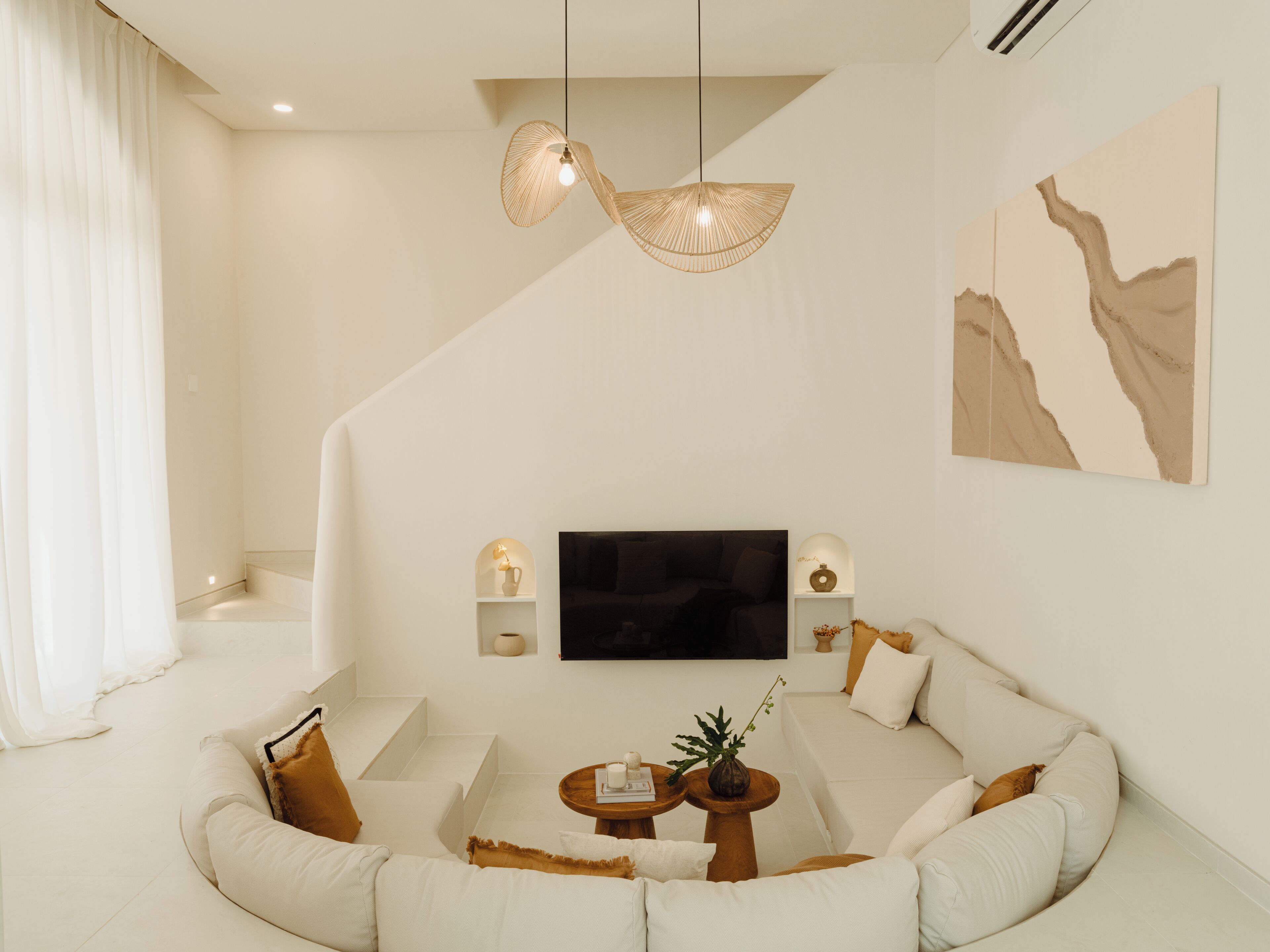Ein modernes Wohnzimmer mit einer gebogenen Couch, einem Flachbildfernseher und einer außergewöhnlichen Pendelleuchte.