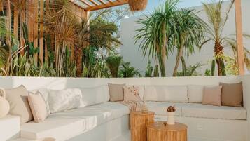 A modern outdoor seating area with a white sofa, two round wooden tables, and a hanging light fixture.