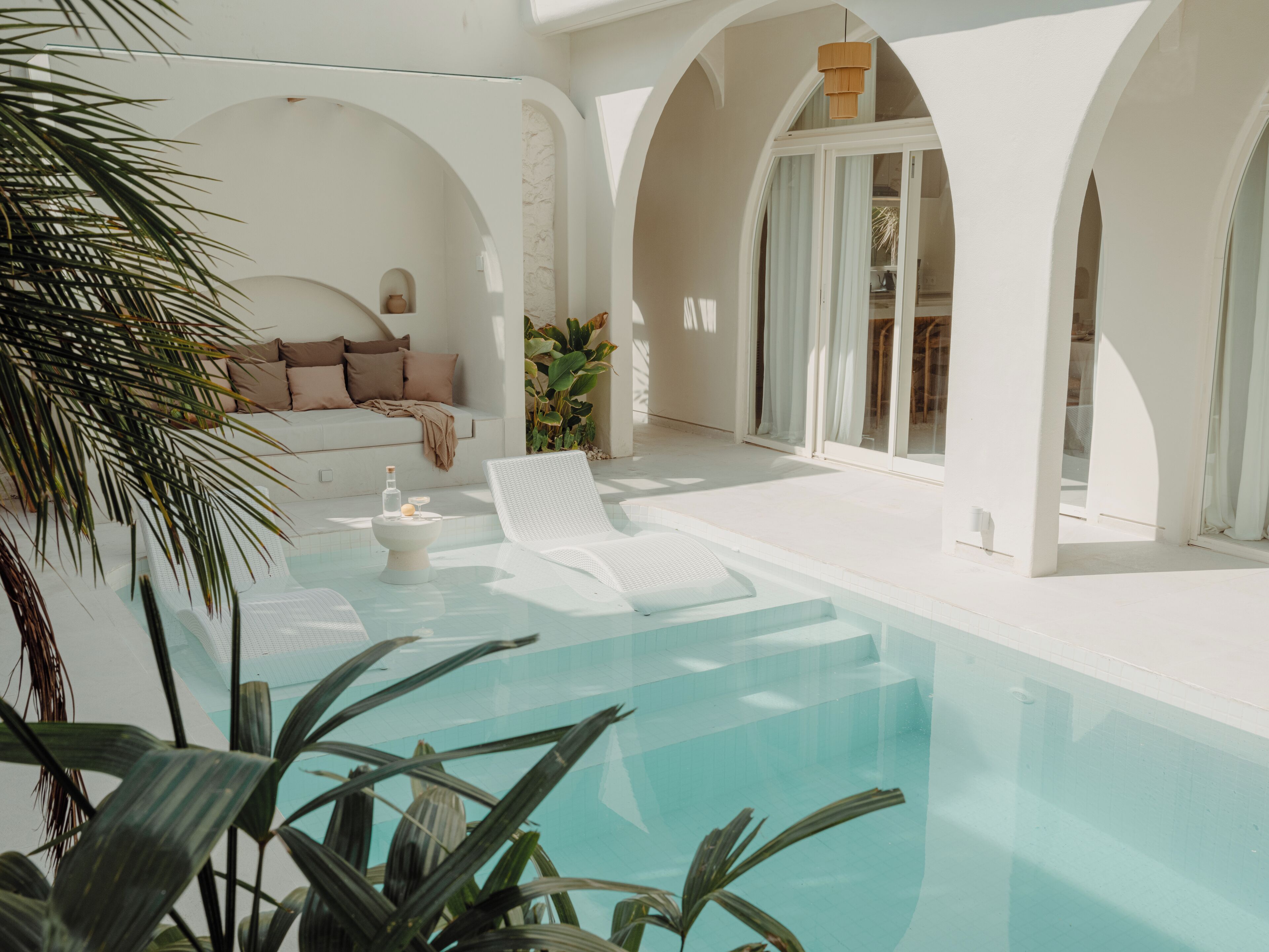 Ein moderner Poolbereich mit einem weißen Infinity-Pool, Liegestühlen und einer Lounge mit Kissen.