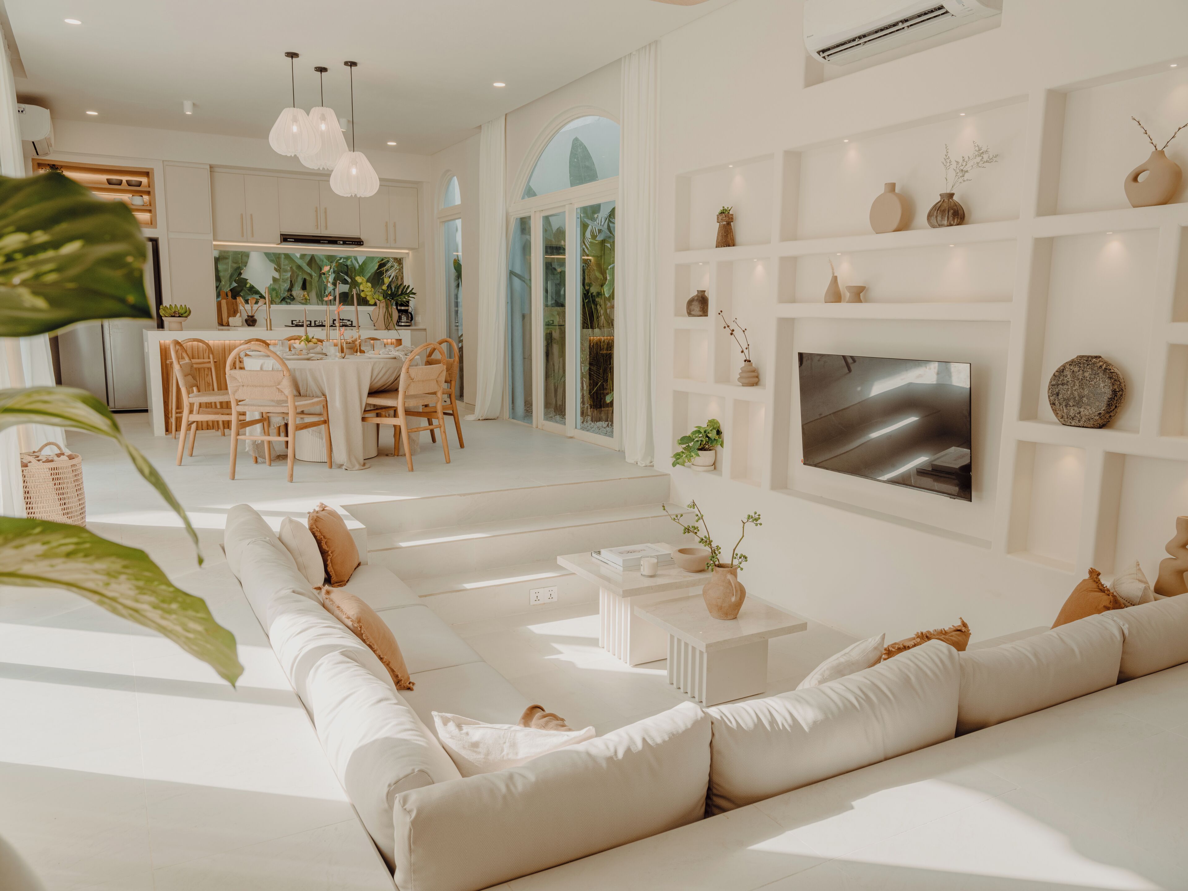 Un salon moderne avec un canapé blanc, un coin repas avec des chaises en bois et un téléviseur fixé au mur.
