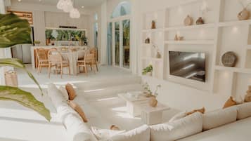 Una sala moderna con un sofá blanco, una zona de comedor con sillas de madera y un televisor montado en la pared.