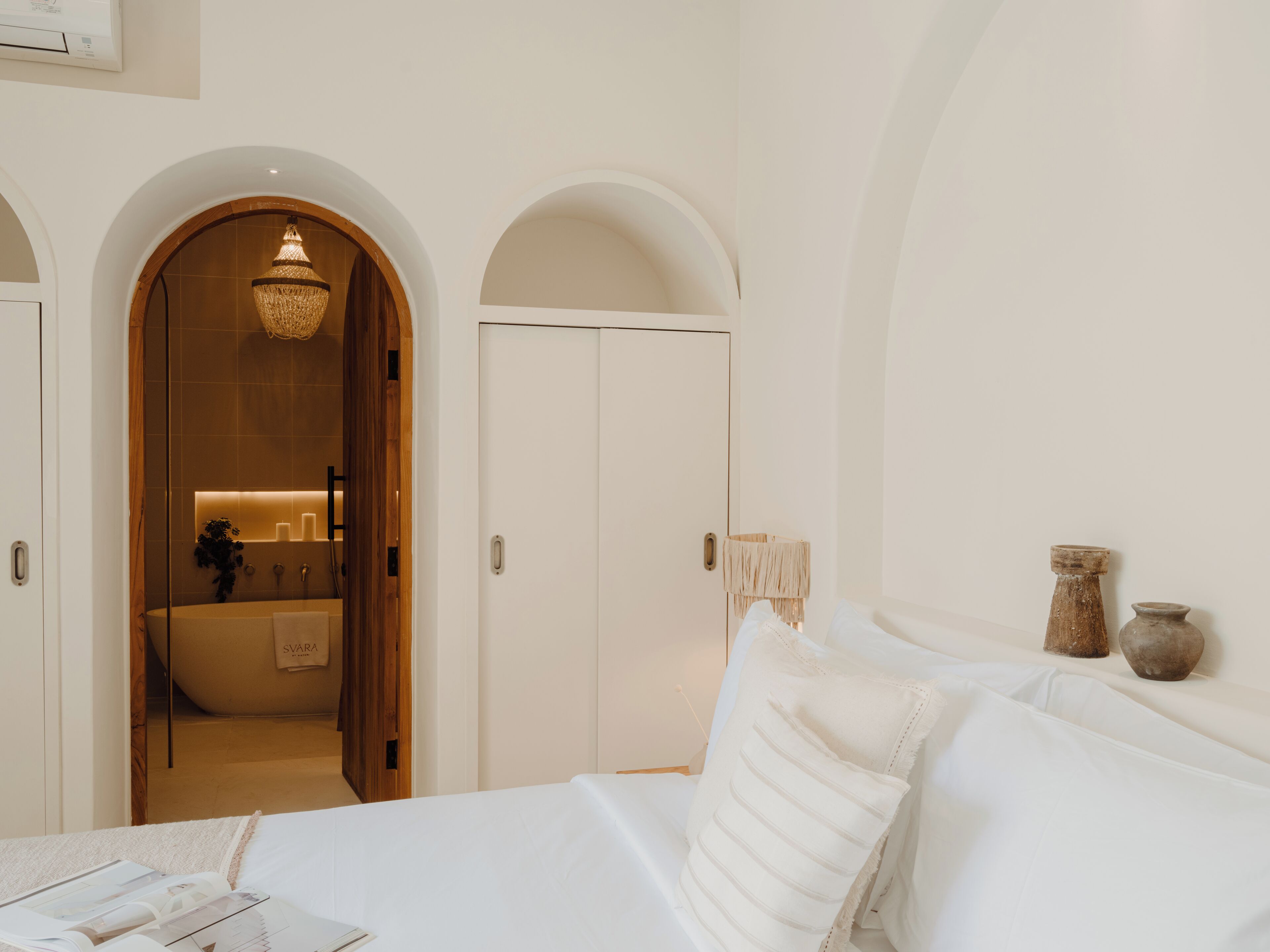 A bedroom with a bed, a wardrobe, and an arched doorway leading to a bathroom.