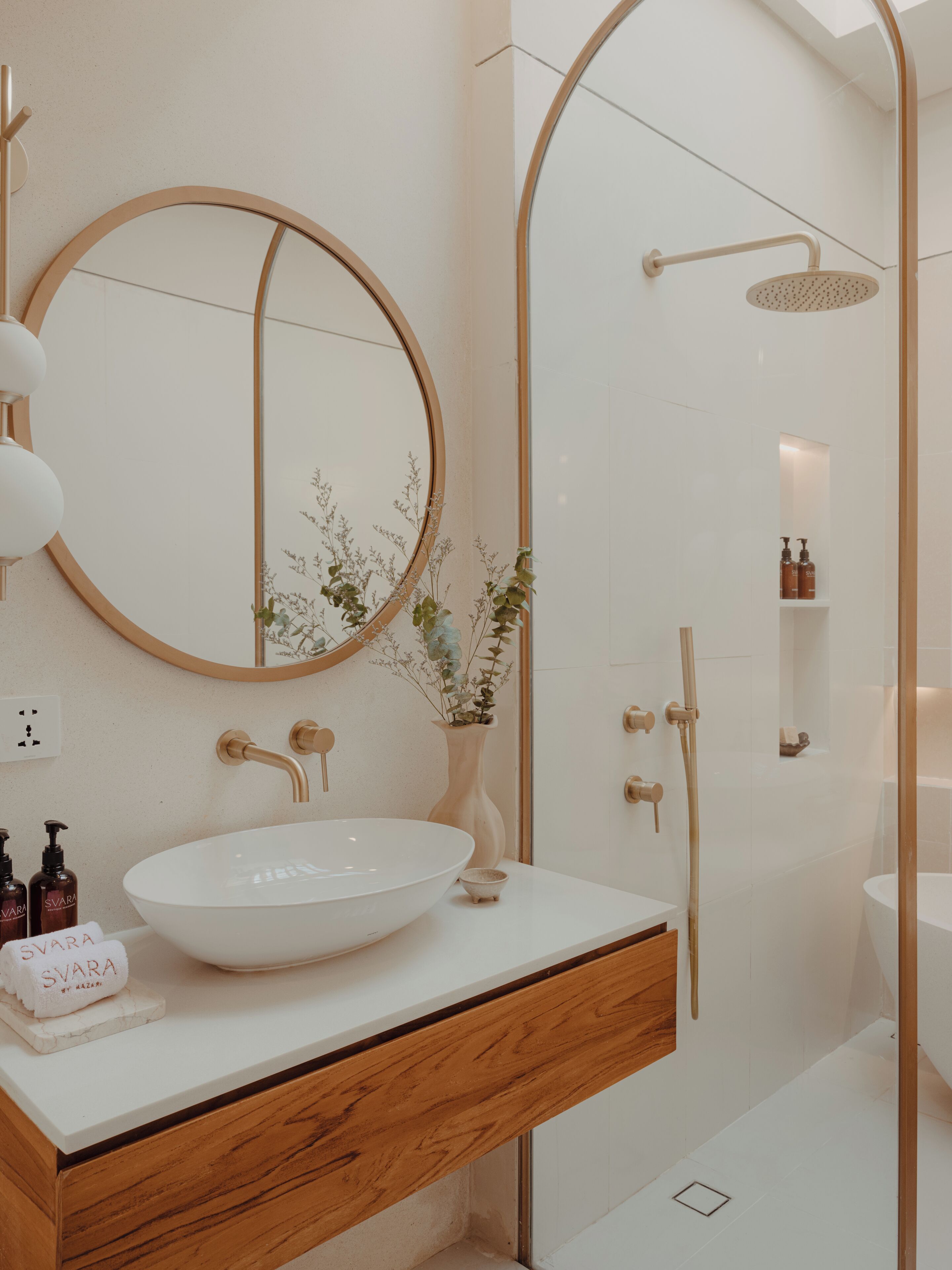 Un bagno moderno con un ampio lavabo ovale, uno specchio rotondo, una doccia dal design curvo e un mobile bagno in legno.