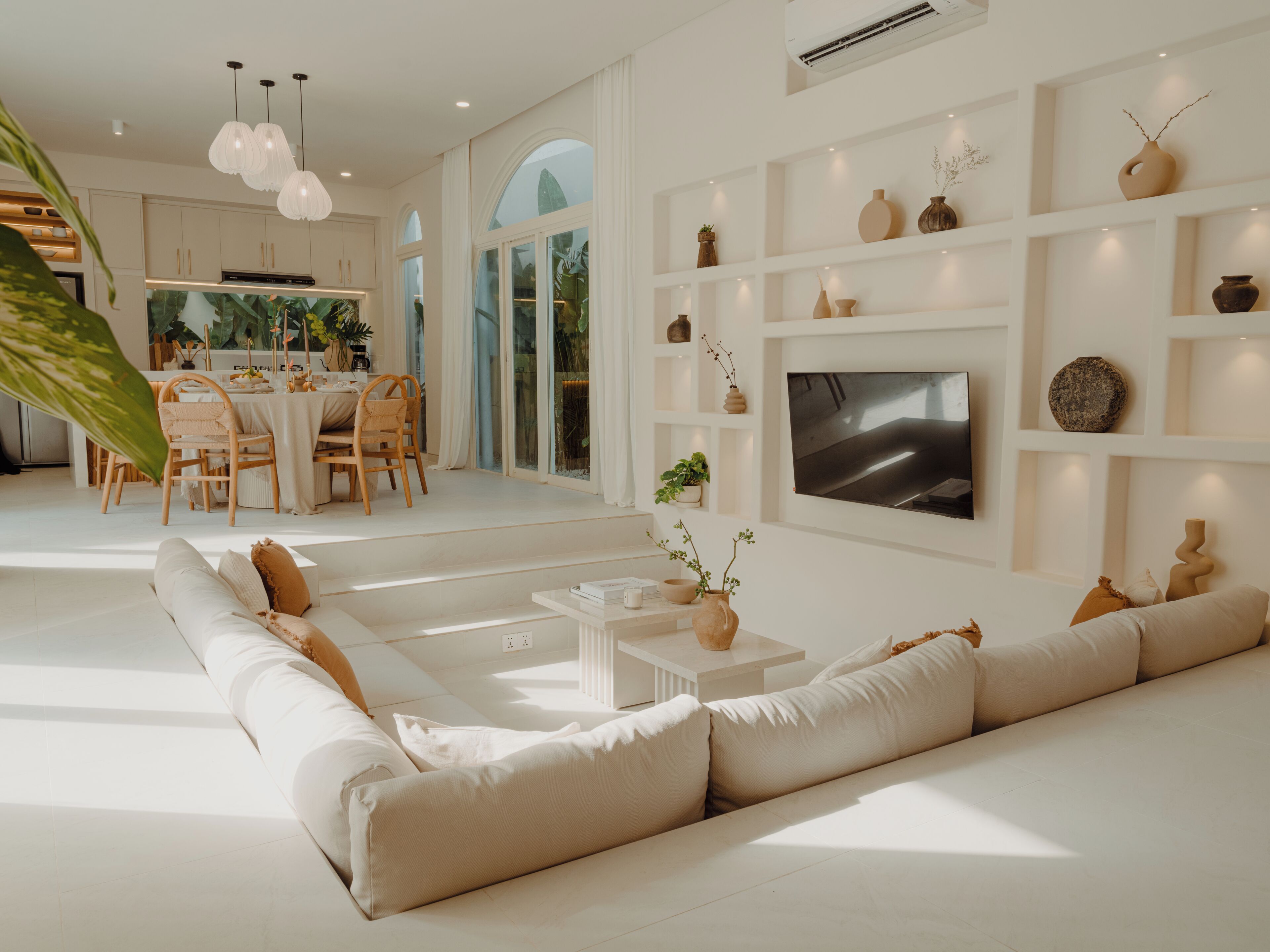 Een moderne woonkamer met een grote bank, een eethoek met een tafel en stoelen, en een aan de muur bevestigde televisie.