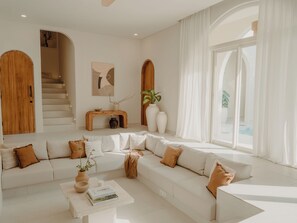 Un salon moderne avec un canapé blanc, une table basse et un escalier menant à l’étage supérieur.