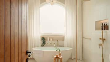 Un baño moderno con una bañera independiente, un cabezal de ducha y un tocador con artículos de aseo.