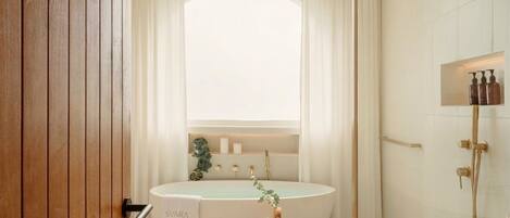 A modern bathroom with a freestanding bathtub, a showerhead, and a vanity with toiletries.
