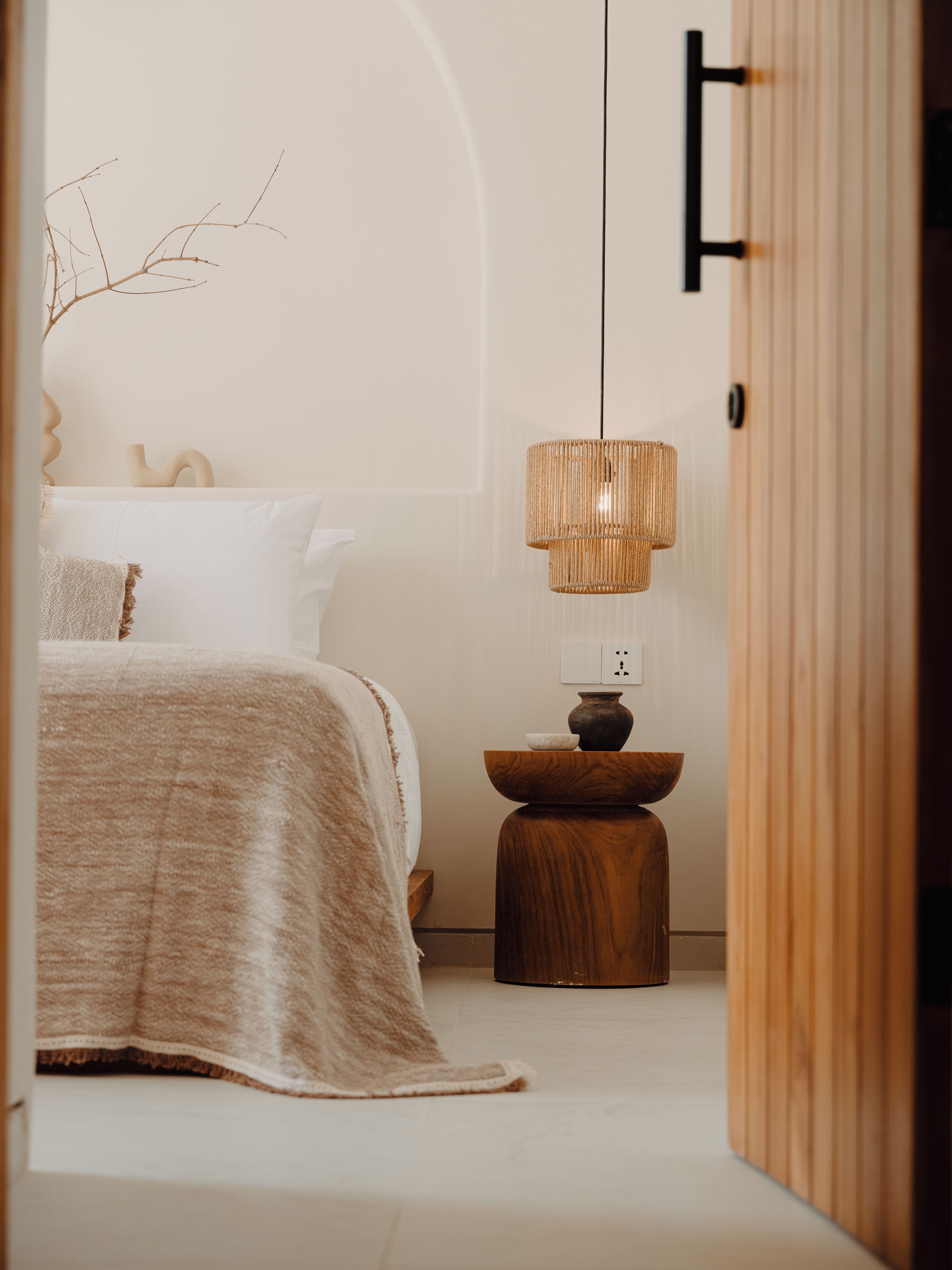 Un dormitorio con cama, una mesita de noche con un florero y una lámpara colgante.