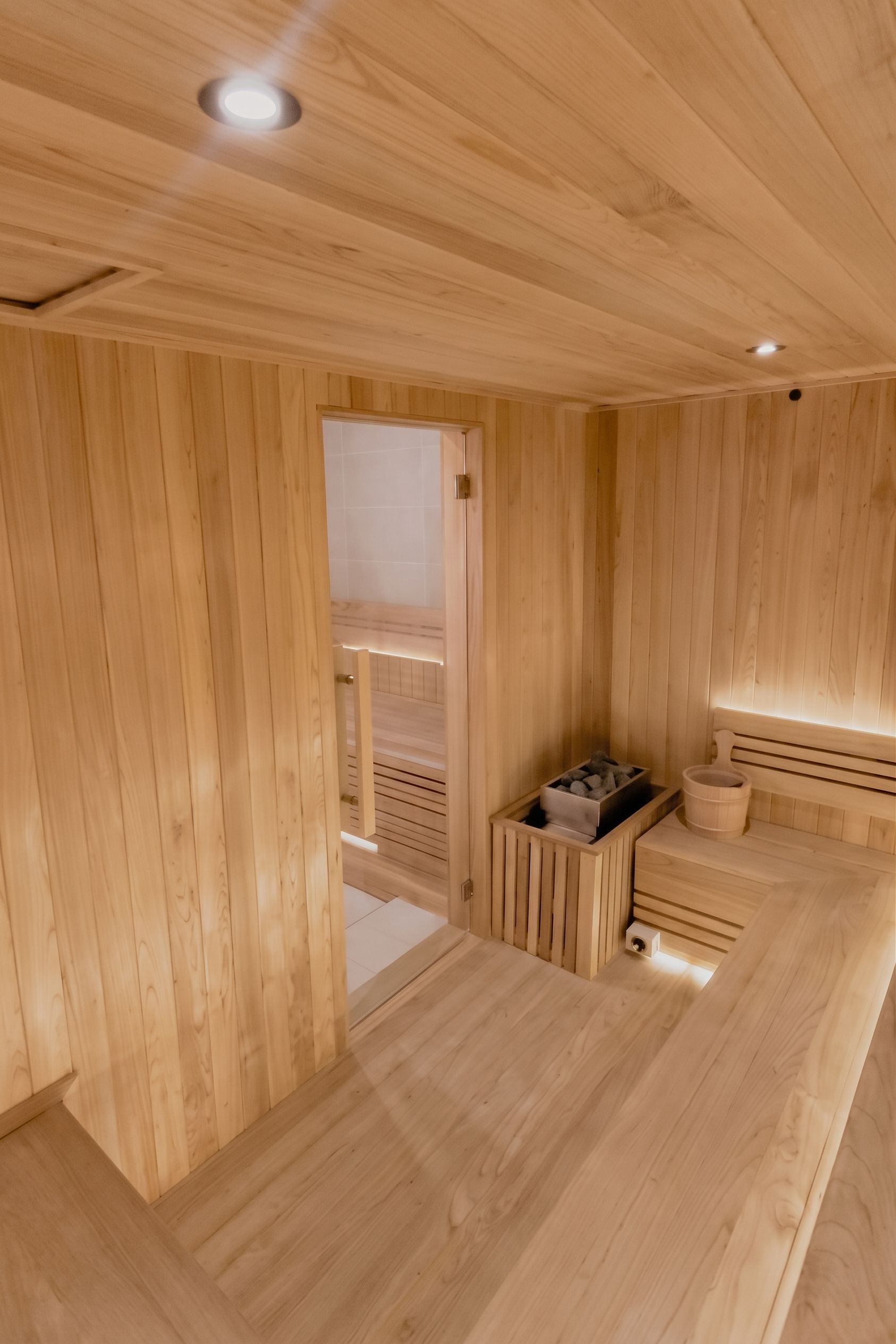 A wooden interior with a sauna area, including a bench and a bucket.