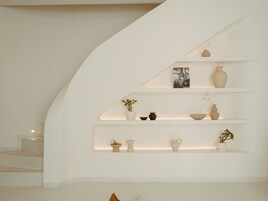 A modern interior with a curved white wall, a staircase, and shelves with decorative items.