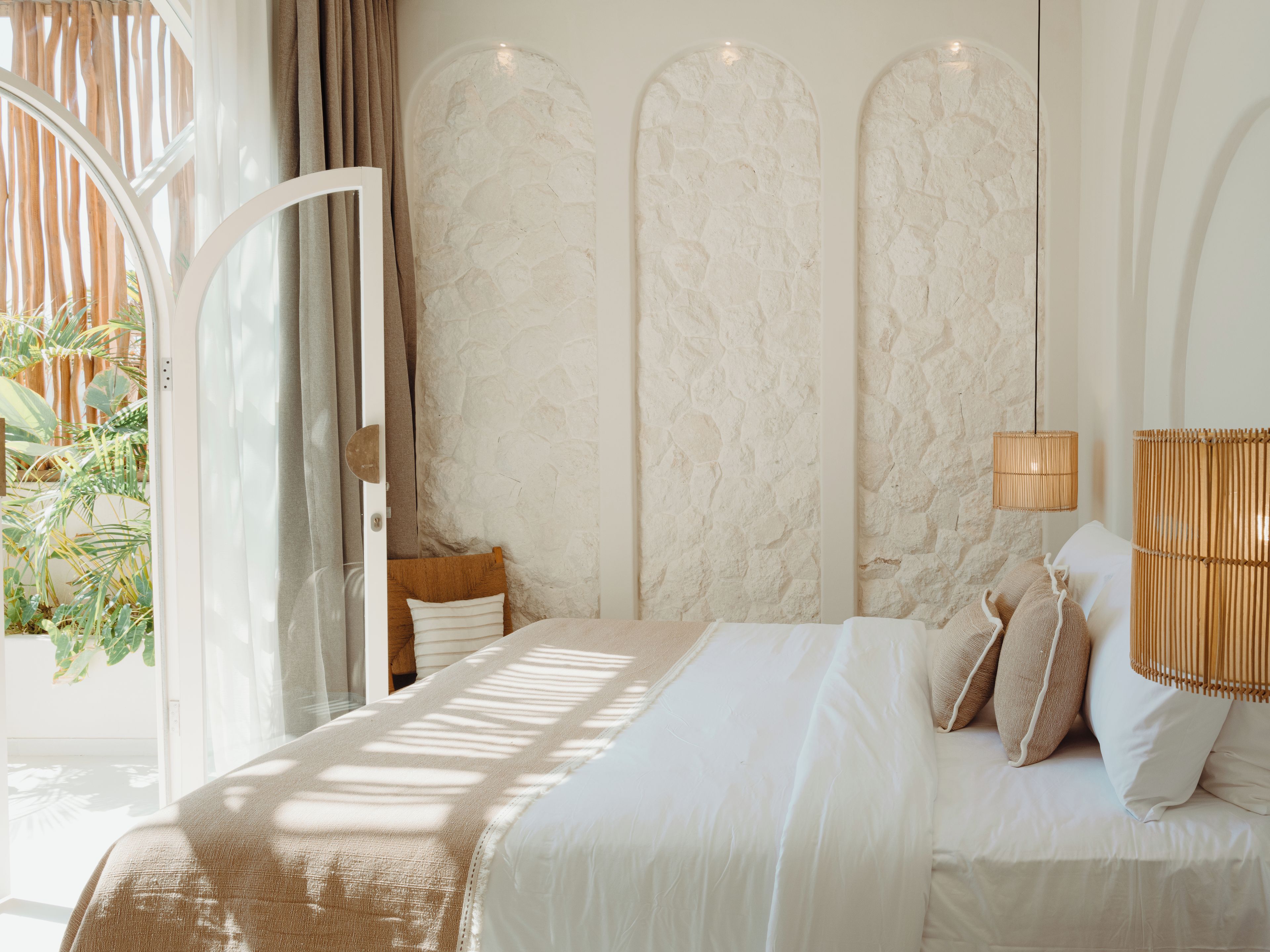 Un dormitorio con cama, almohadas, una lámpara colgante y vistas al exterior.