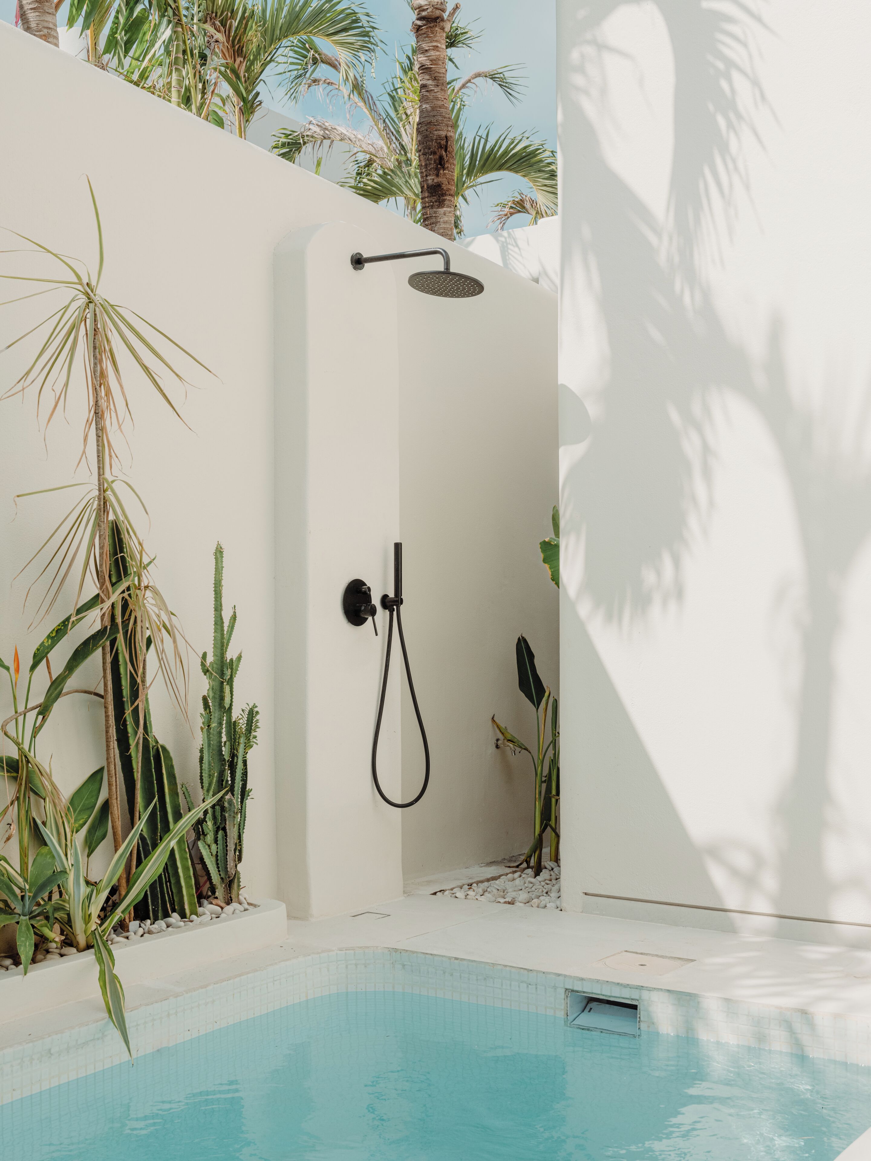 Ducha exterior moderna con cabezal de ducha tipo lluvia, rodeada de plantas y una piscina.