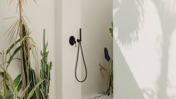 Ducha exterior moderna con cabezal de ducha tipo lluvia, rodeada de plantas y una piscina.