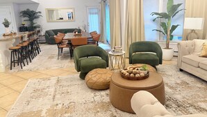 Amplia sala de estar con una gran mesa de comedor, sillones verdes, un sofá color beige y una mesa de centro con objetos decorativos.