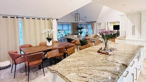 Una cocina amplia con una isla grande, un comedor con mesa y sillas de madera, y una sala de estar con sofá y televisor.