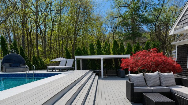 Una terraza de madera con piscina, mobiliario exterior y un área cubierta.