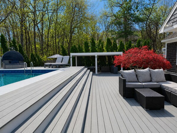 A wooden deck with a pool, outdoor seating, and a covered area.