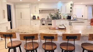 Una cocina moderna con armarios blancos, una isla grande con taburetes de bar y una planta en el centro.