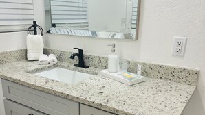 A bathroom with a granite countertop, a sink, a mirror, and a towel rack.