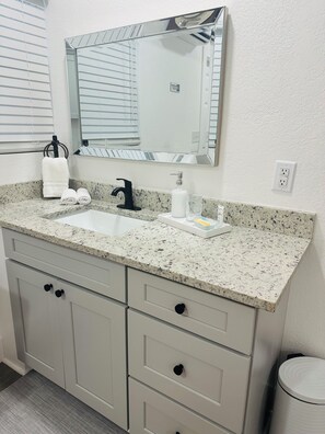 A bathroom with a granite countertop, a sink, a mirror, and a towel rack. - Welcome to the Spring Dream (High Springs)