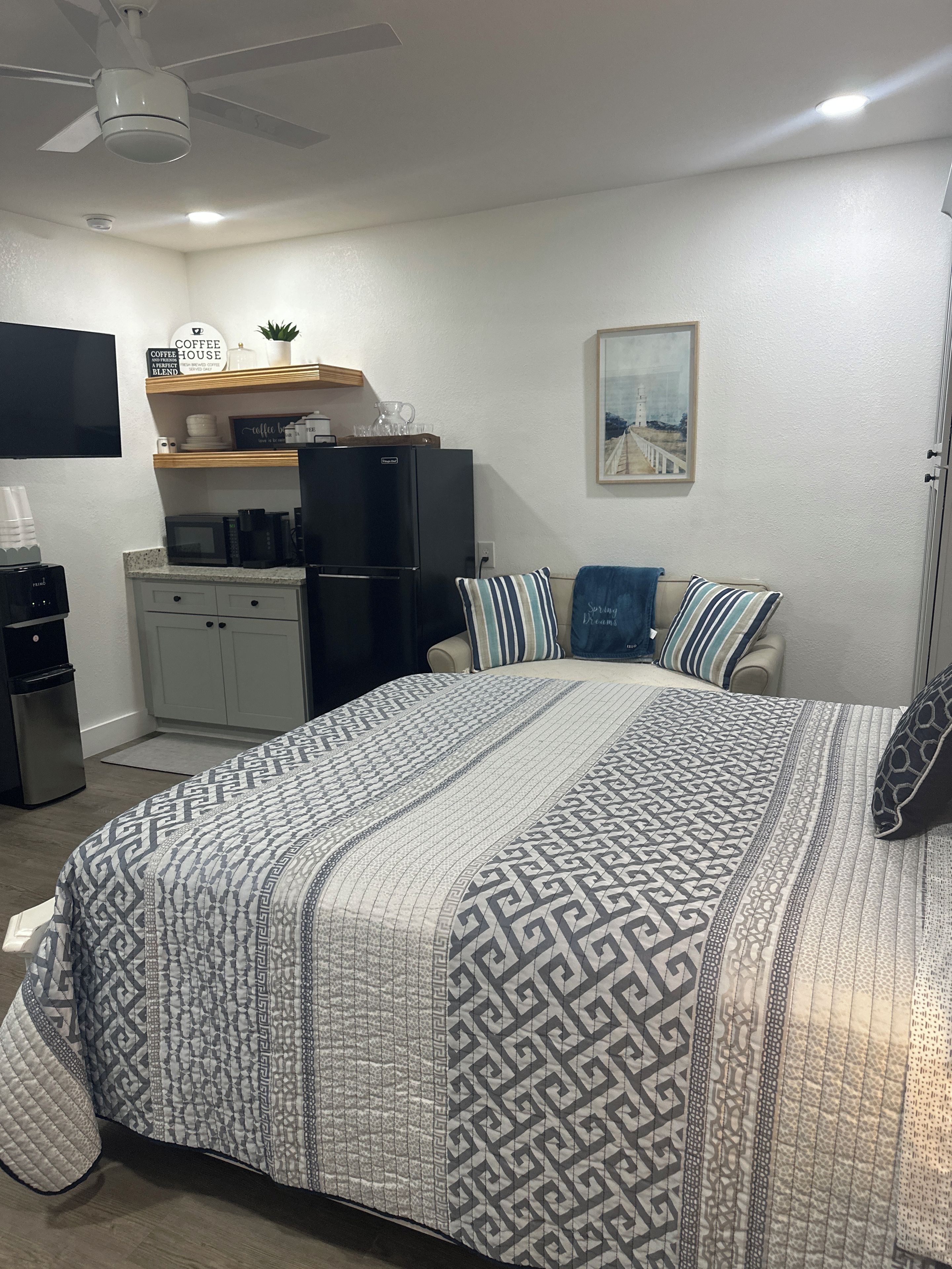 Une chambre à coucher comprenant un lit, une table basse, un réfrigérateur, un four à micro-ondes et un ventilateur de plafond.