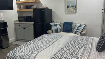 Une chambre à coucher comprenant un lit, une table basse, un réfrigérateur, un four à micro-ondes et un ventilateur de plafond.