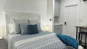 A neatly made bed with patterned bedding, a bedside table with a lamp, and a small table with a plate and a cup.