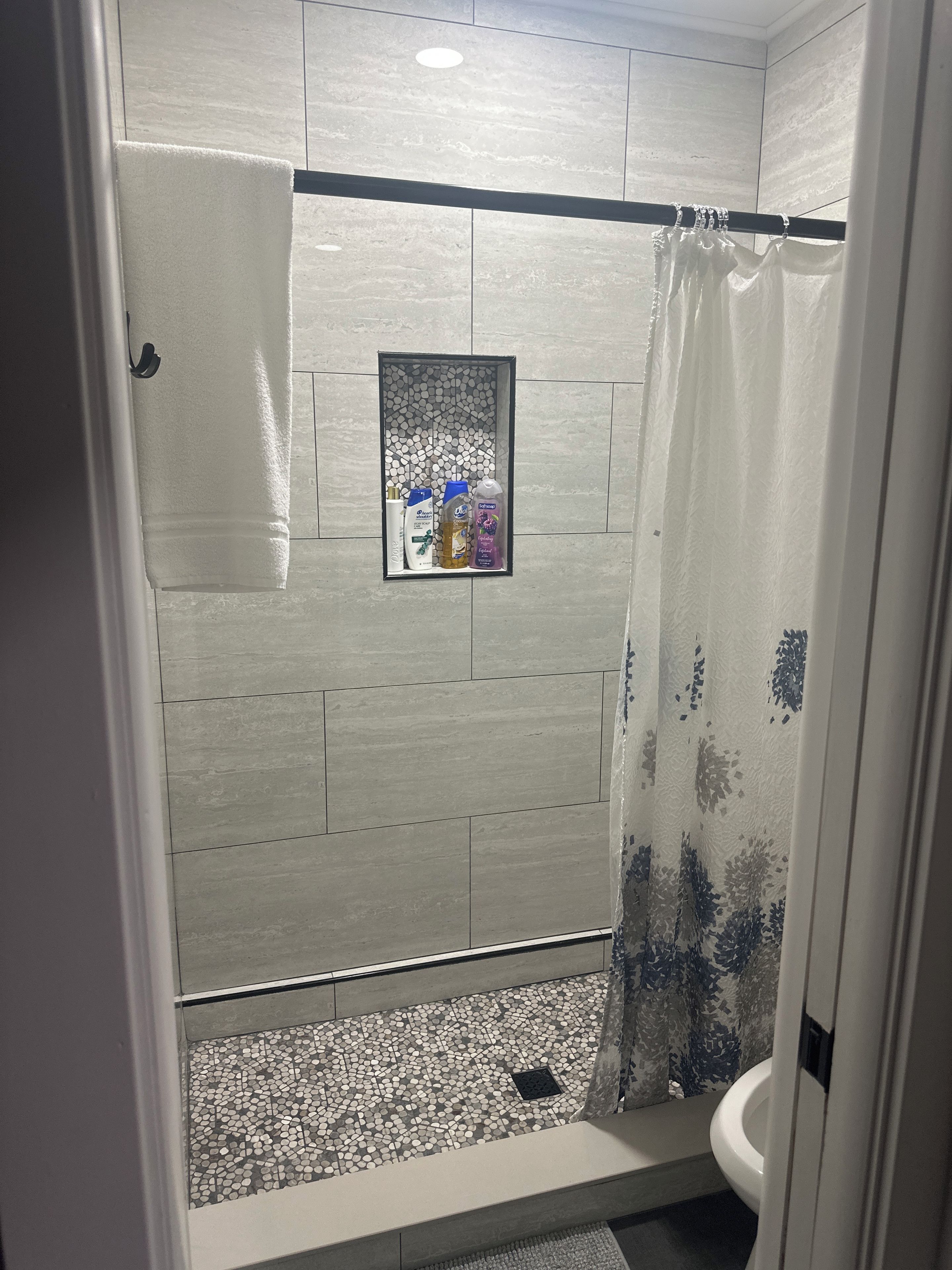 A bathroom with a shower area, a toilet, and a shelf with toiletries.