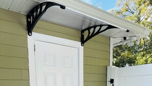 A white door with a black handle, a brown doormat, and a white fence.