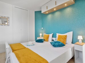 Une chambre à coucher moderne avec un mur d’accent de couleur turquoise, un lit blanc agrémenté d’oreillers jaunes et bleus, et une tête de lit en bois.
