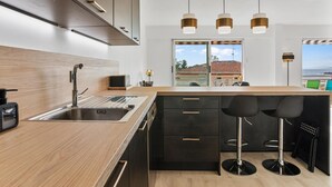 A modern kitchen with a wooden countertop, black cabinets, a stainless steel sink, and a bar area with stools. - 4* - sea view - 2 bedrooms - parking - swimming pool (Saint-Raphaël)