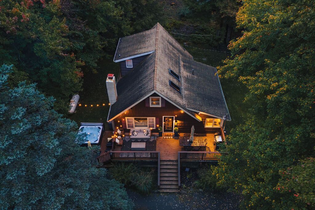 A wooden cabin with a deck, a hot tub, and string lights.