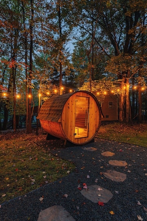 A wooden barrel-shaped cabin with a door open, surrounded by trees and string lights. - Game Room Fun ~Hot Tub ~Sauna ~Fall Lake Adventure ~Dog Friendly (Pocono Lake)