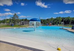 Ein Schwimmbecken mit einer Springbrunnenanlage, umgeben von einem Zaun und Bäumen.