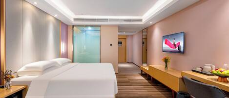 A modern hotel room with a large bed, a desk with a chair, a television, and a dining area with a table and chairs.