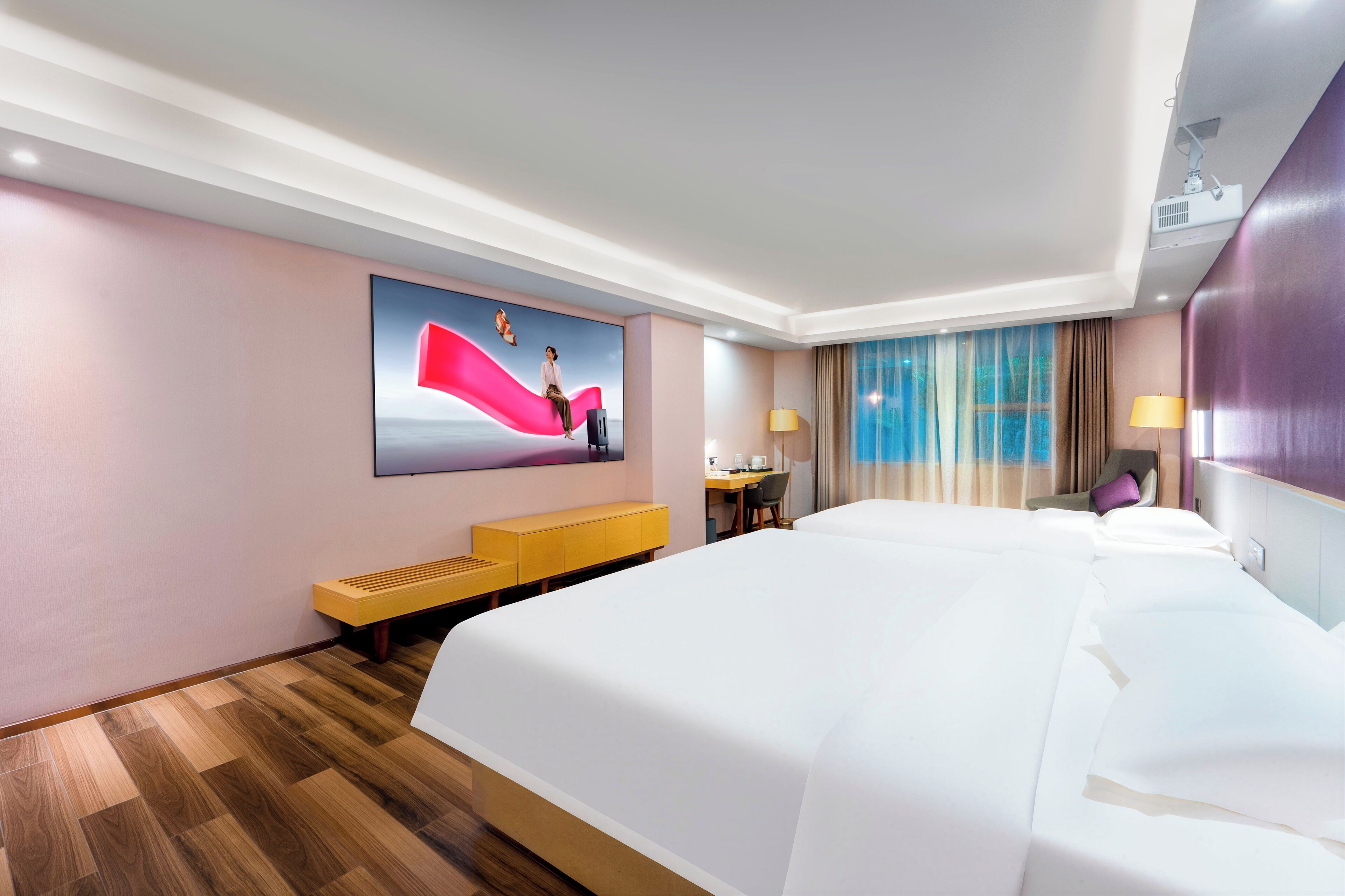 Een hotelkamer met een groot bed, een bureau, een stoel, een bankje en een aan de muur bevestigde televisie.