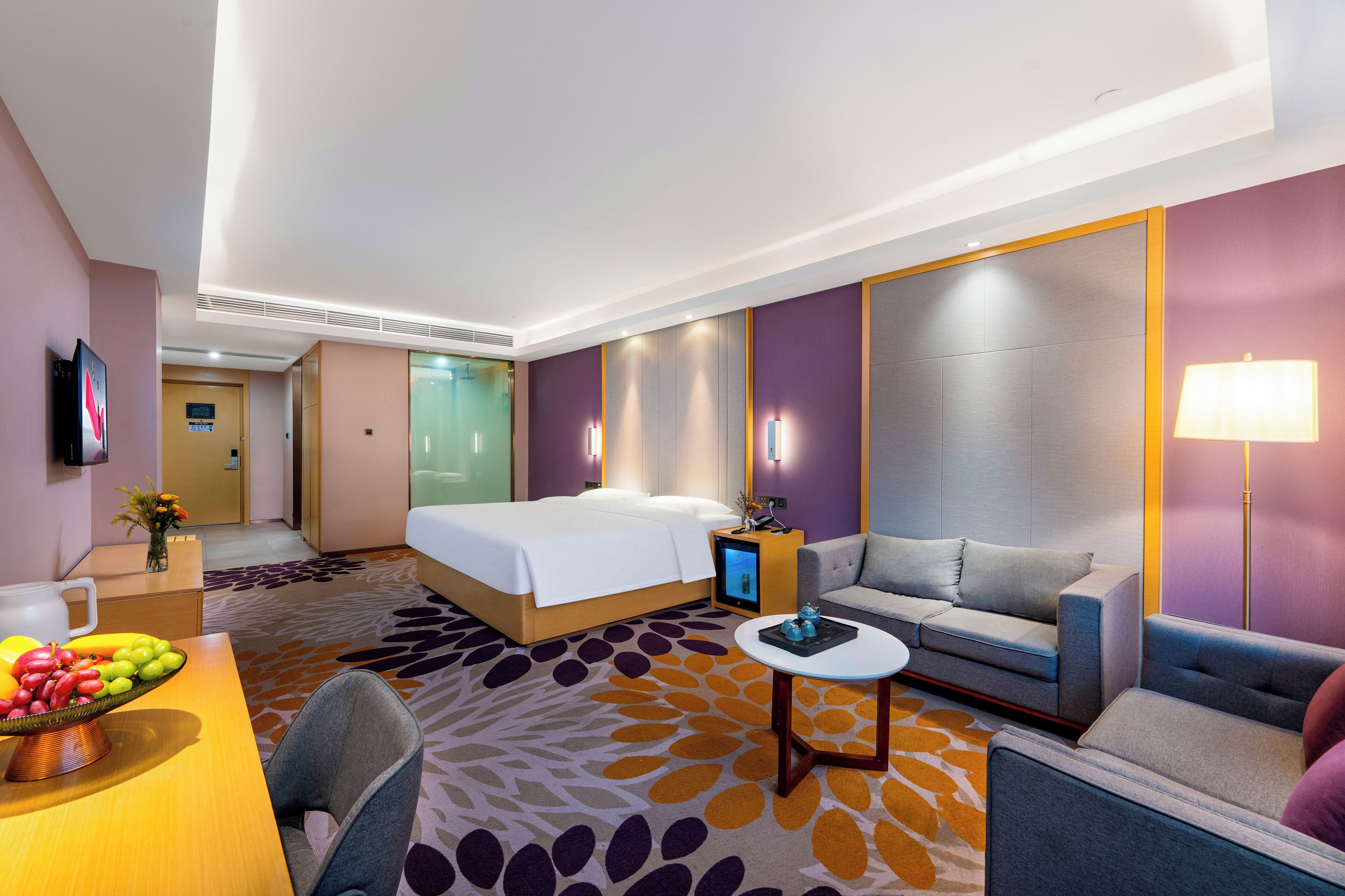 Una habitación de hotel con cama, sofá, sillón, una mesita y un frutero.