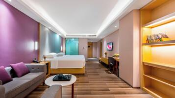 Quarto de hotel moderno com cama, sofá, mesa de centro e televisão.